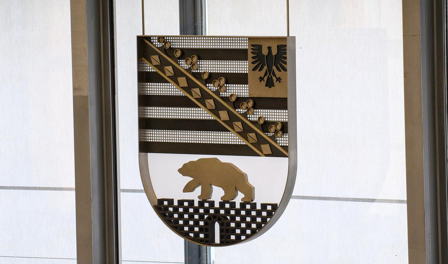 KI generiert: Das Bild zeigt ein Wappen mit einem schwarzen Adler auf goldenem Grund in der oberen Hälfte und einem goldenen Bären auf schwarzem Grund in der unteren Hälfte. Der Hauptinhalt des Bildes ist das Wappen, das zwischen zwei Fenstern hängt.