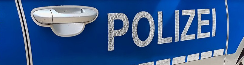 KI generiert: Das Bild zeigt die seitliche Aufschrift "POLIZEI" auf einem blauen Polizeifahrzeug in Deutschland. Der Fokus liegt auf dem Türgriff und der Beschriftung auf der Autotür.