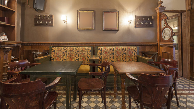 KI generiert: Das Bild zeigt den Innenraum eines gemütlichen Cafés oder Restaurants mit Holzmöbeln, einer gepolsterten Bank und beleuchteten Wänden. Die Atmosphäre wirkt einladend und traditionell.