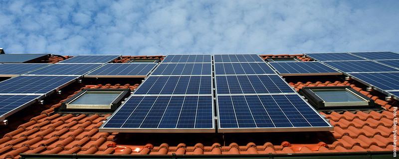 KI generiert: Das Bild zeigt ein Dach mit mehreren installierten Solarmodulen unter einem leicht bewölkten Himmel. Die Solarmodule sind auf einem rot gedeckten Ziegeldach montiert.