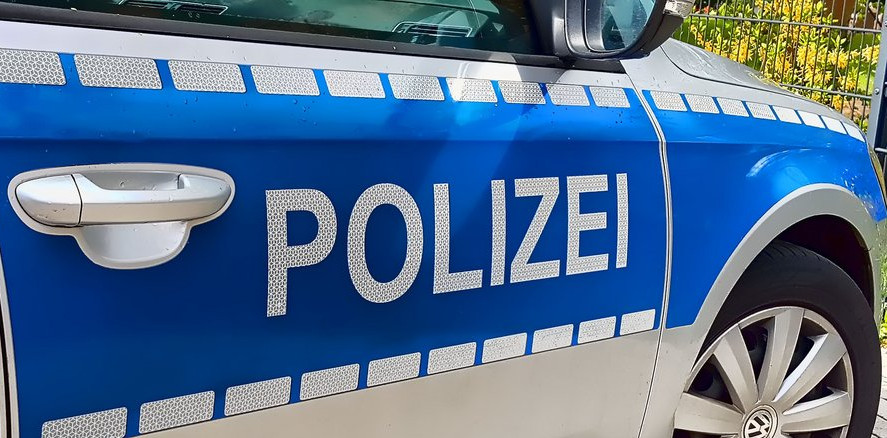 KI generiert: Das Bild zeigt die Seite eines blauen Polizeiautos mit der Aufschrift "POLIZEI". Der Schwerpunkt liegt auf dem Schriftzug und einem Teil der Fahrzeugtür und des Rades.