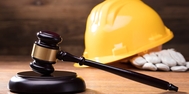 KI generiert: Das Bild zeigt einen Richterhammer neben einem gelben Bauhelm und Arbeitshandschuhen auf einem Tisch. Es symbolisiert die Verbindung von Recht und Bauarbeit.