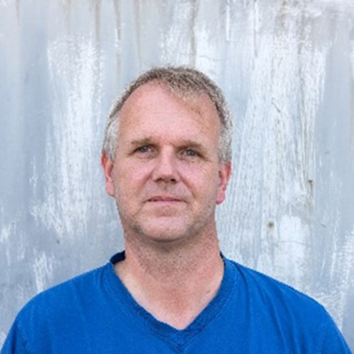 KI generiert: Das Bild zeigt einen Mann in einem blauen Hemd vor einem hellen, strukturierten Hintergrund. Der Fokus liegt auf dem Gesicht des Mannes.