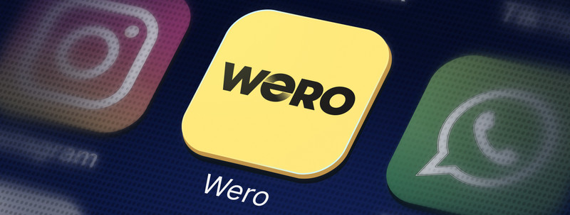 KI generiert: Das Bild zeigt ein gelbes App-Icon mit der Aufschrift "Wero" auf einem Bildschirm mit anderen bekannten App-Symbolen. Im Hintergrund sind die Icons von Instagram und WhatsApp erkennbar.