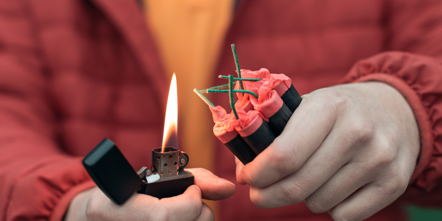 KI generiert: Das Bild zeigt eine Person, die mit einem Feuerzeug eine Gruppe von Feuerwerkskörpern entzünden möchte. Der Fokus liegt auf den Feuerwerkskörpern und der offenen Flamme des Feuerzeugs.