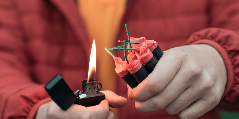 KI generiert: Das Bild zeigt eine Person, die mit einem Feuerzeug eine Gruppe von Feuerwerkskörpern entzünden möchte. Der Fokus liegt auf den Feuerwerkskörpern und der offenen Flamme des Feuerzeugs.