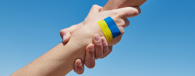 KI generiert: Das Bild zeigt zwei Hände, die sich festhalten, wobei eine Hand ein blau-gelbes Armband trägt. Der Hauptinhalt des Bildes ist die symbolische Darstellung von Unterstützung oder Solidarität, möglicherweise in Bezug auf die Ukraine, deren Nationalfarben Blau und Gelb sind.
